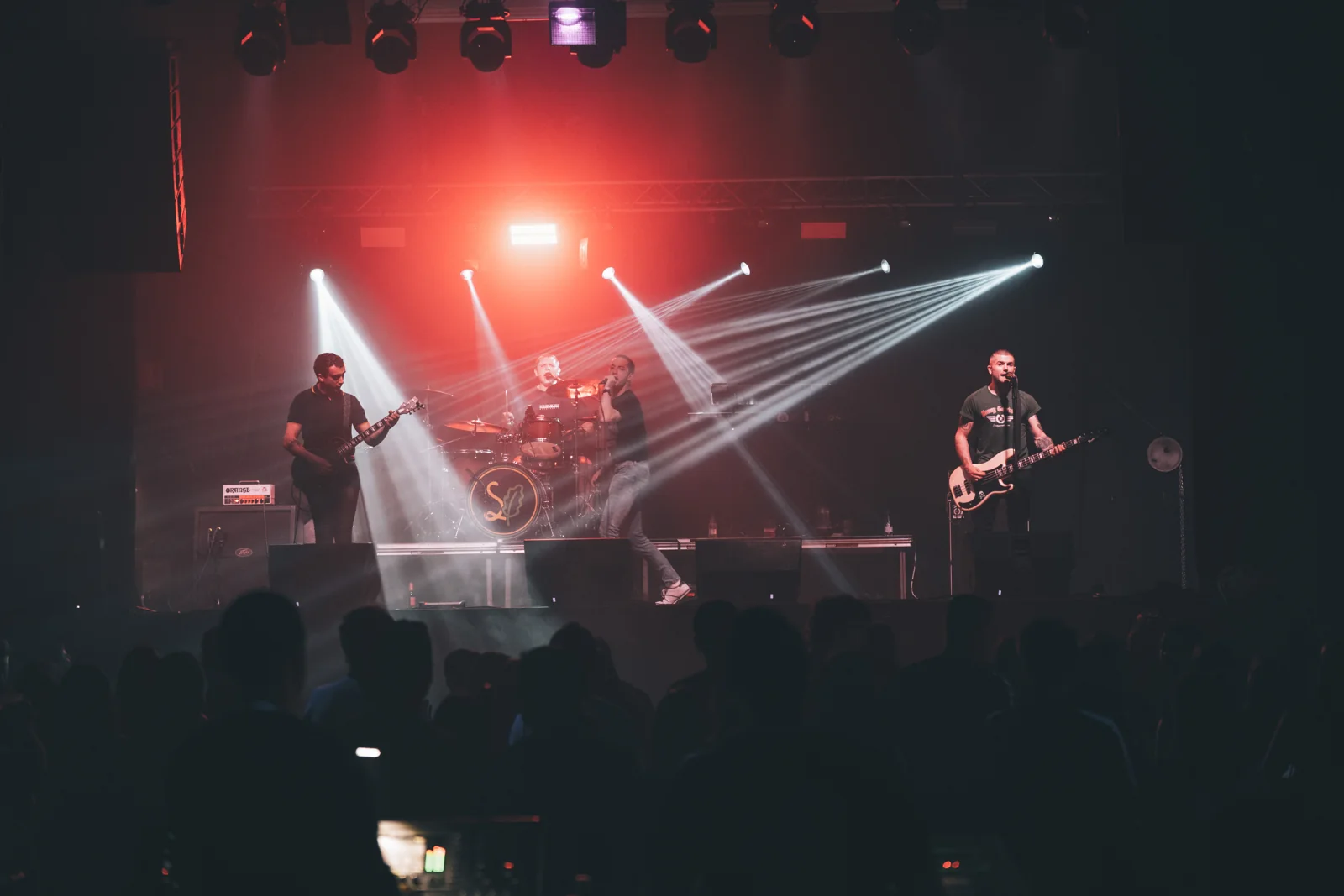 Vista completa de un concierto de Skabidean con haces blancos y fondo rojo en el escenario.