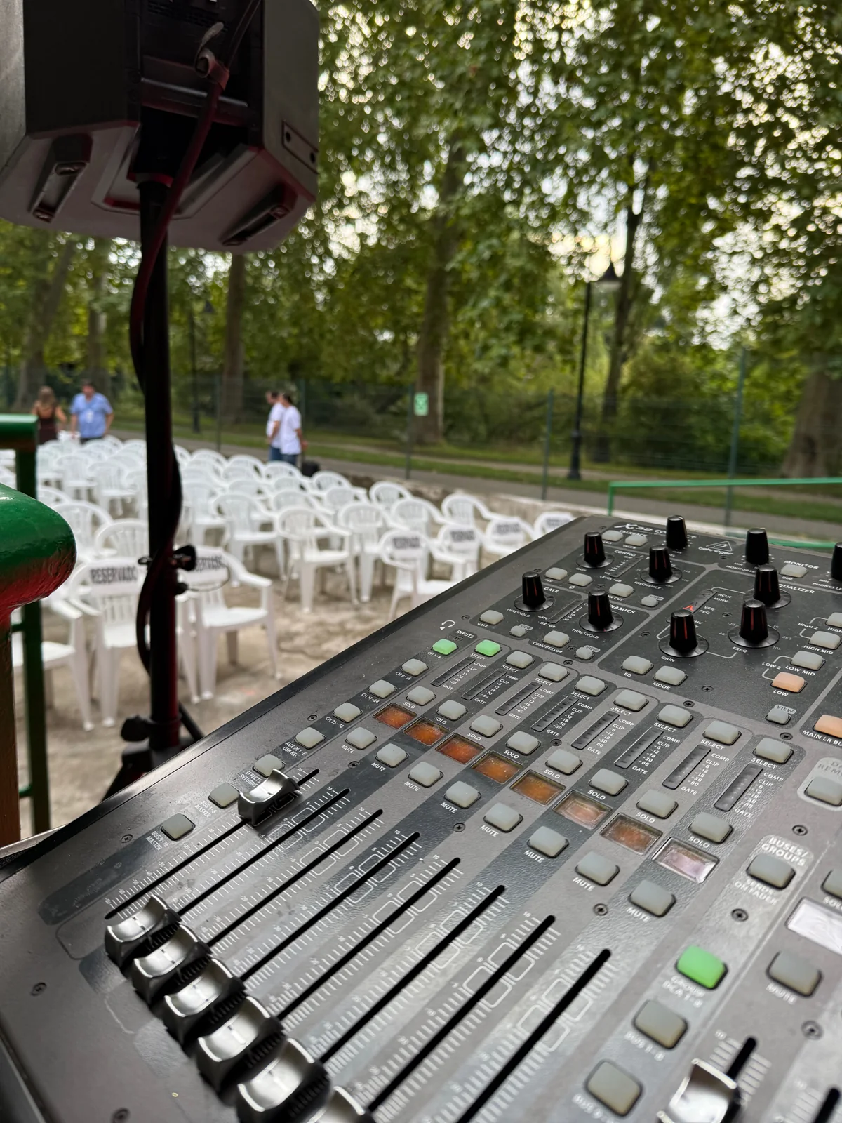 Mesa de mezcla y sistema de sonido preparados junto a las sillas de un evento al aire libre.